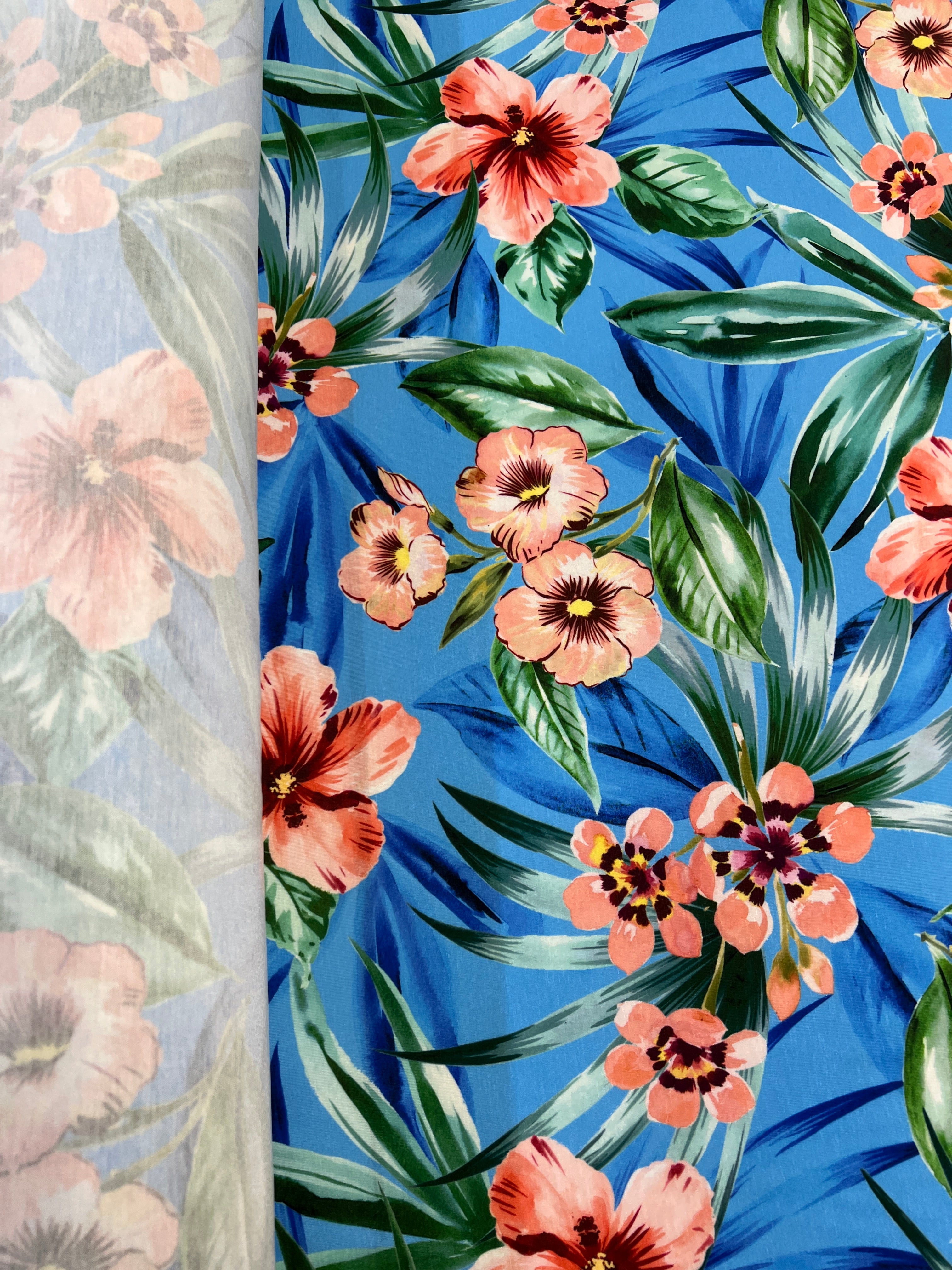 Tropical floral pattern with pink flowers and green leaves on a blue background.