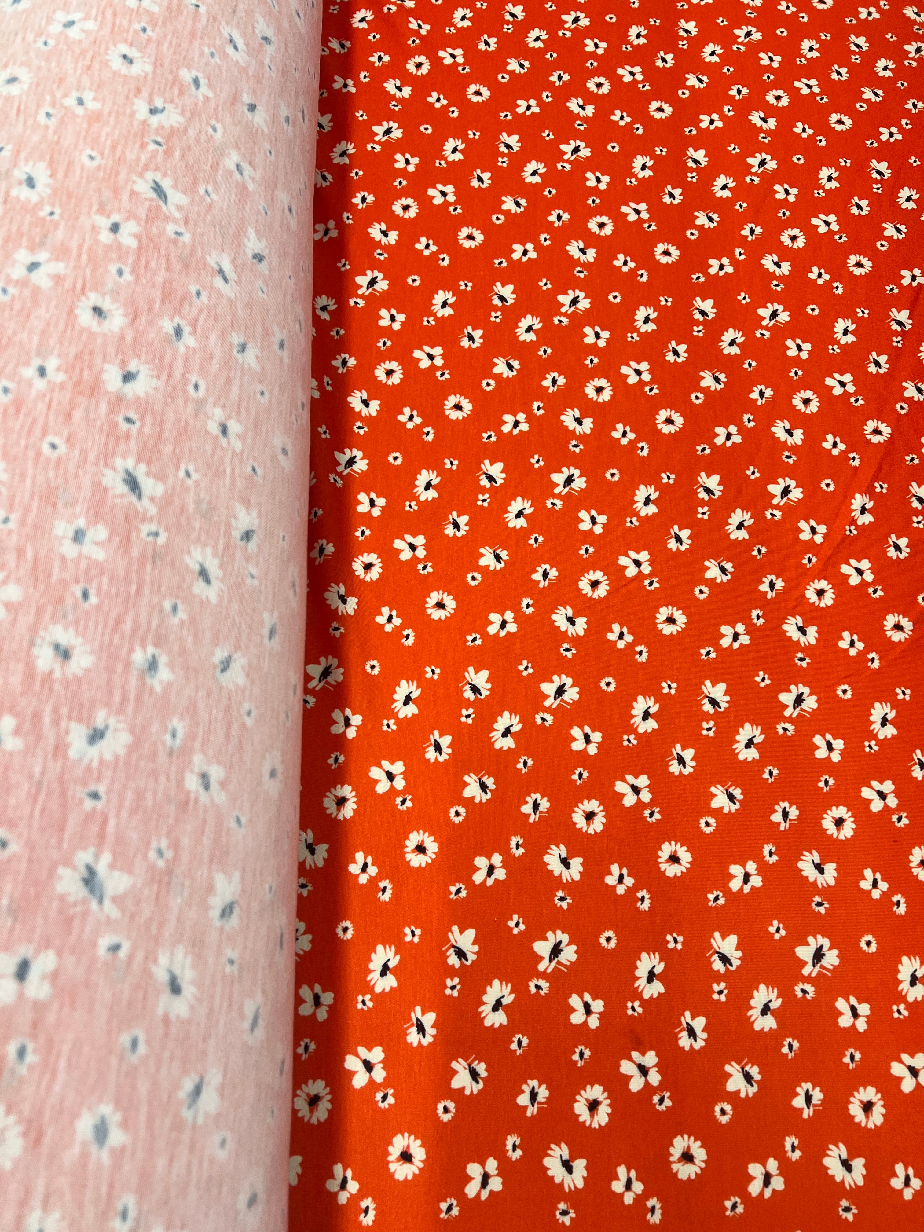 Floral patterned fabric with small white flowers on a red-orange background