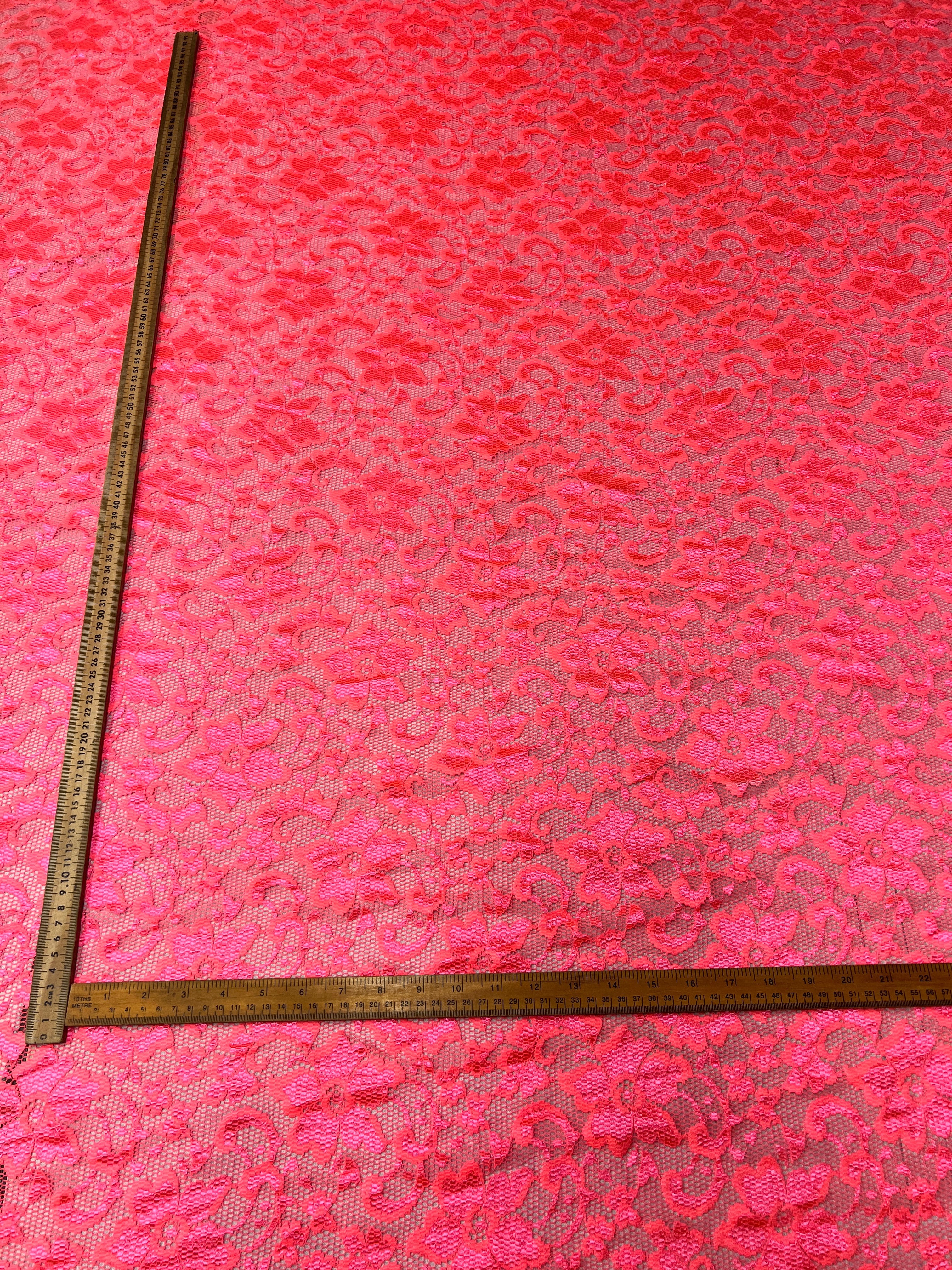Pink lace fabric with a ruler for scale on a pink background