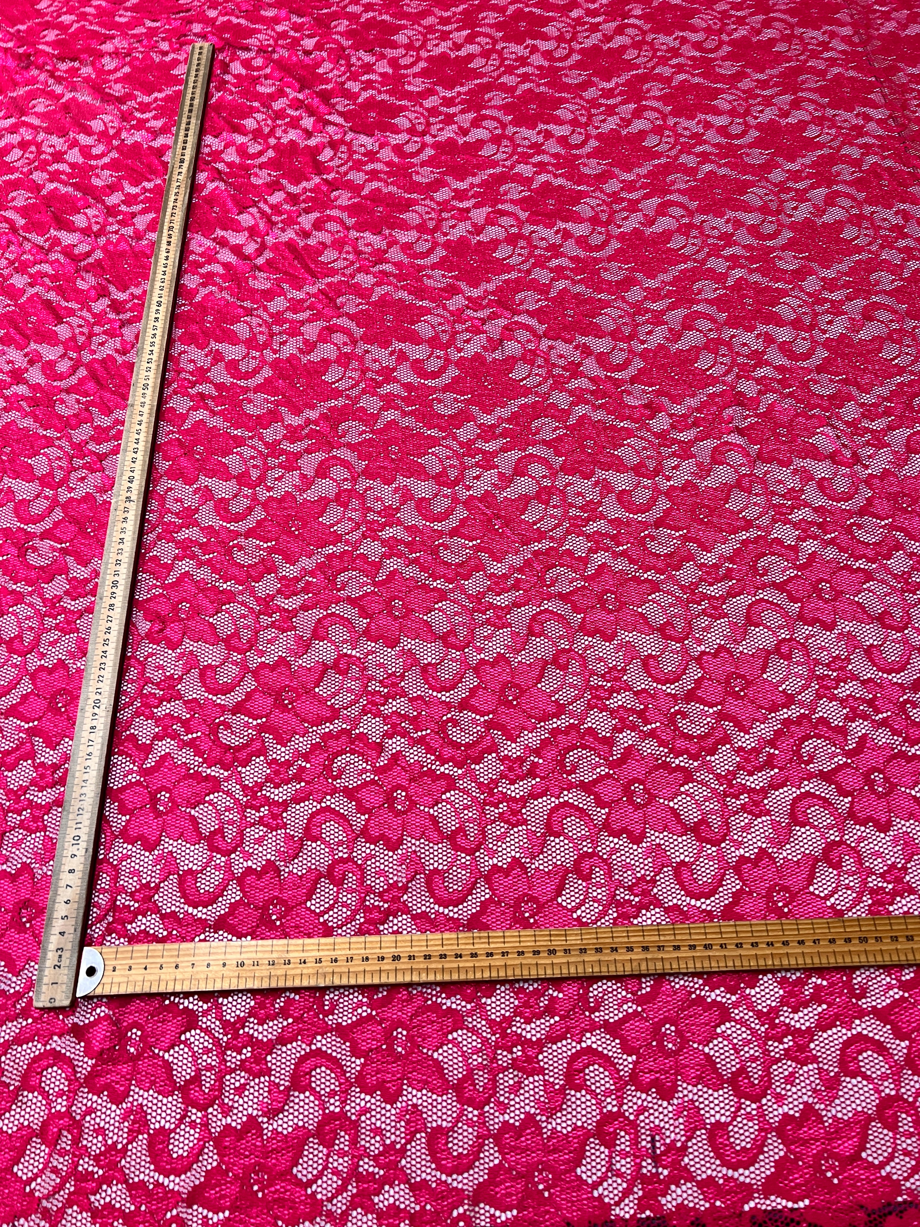 Pink lace fabric with a ruler for scale on a pink background