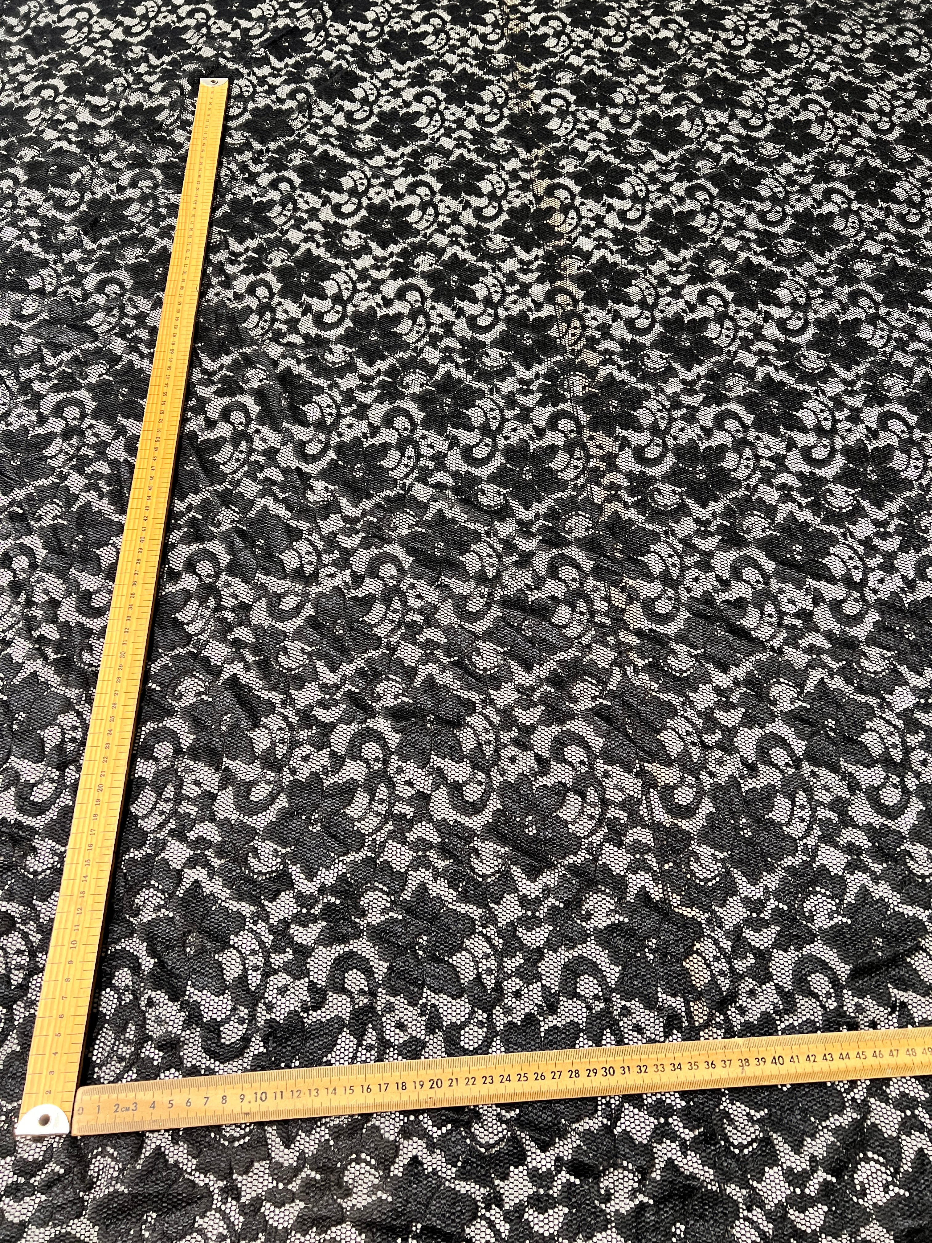Black and white floral lace fabric with a measuring tape for scale.