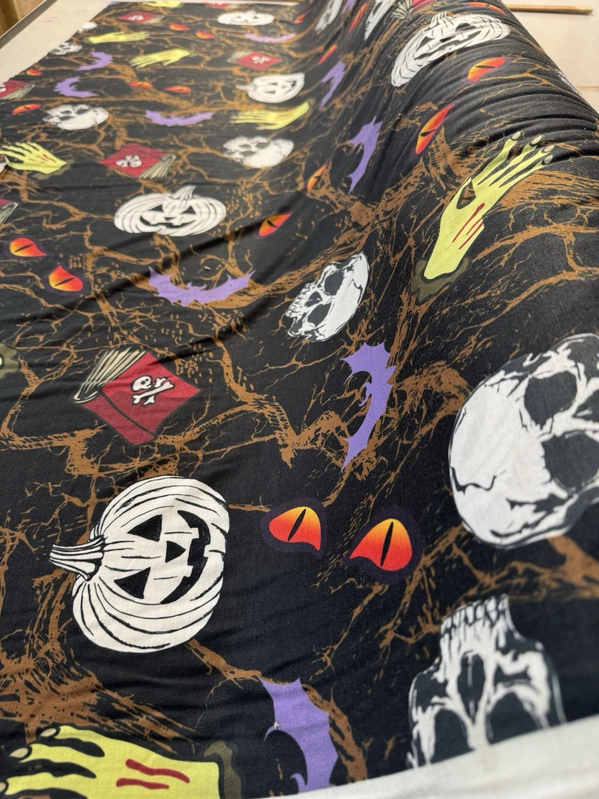 Halloween-themed fabric with pumpkins, ghosts, and skeletons on a black background.